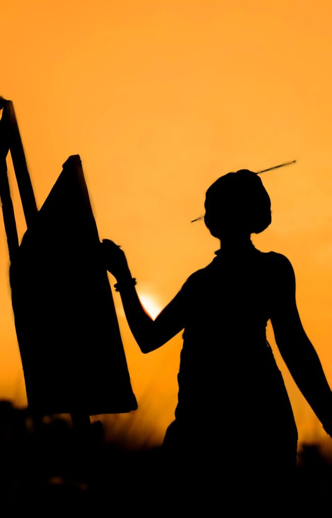 A painter silhouetted at an easel against a golden sunset.
