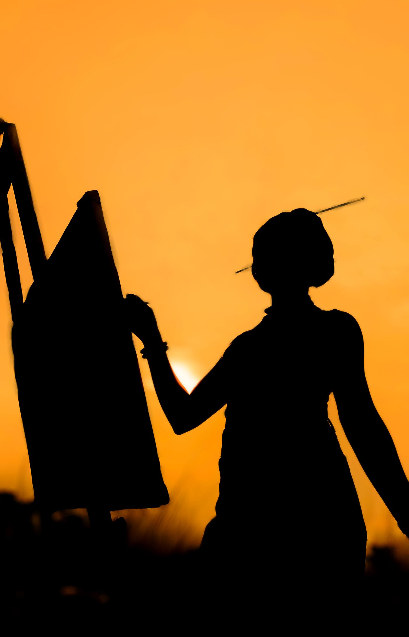 A painter silhouetted at an easel against a golden sunset.